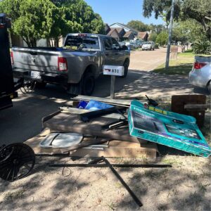 A pile of household junk, including a large Hisense TV box and metal frames, piled by the curb for removal.